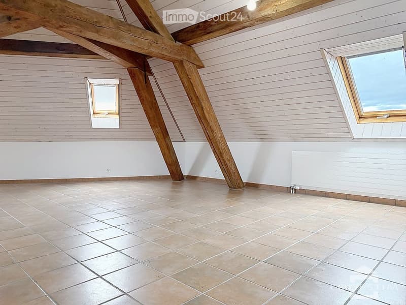 Empty attic room with exposed wooden beams, tiled floor, and skylights.
