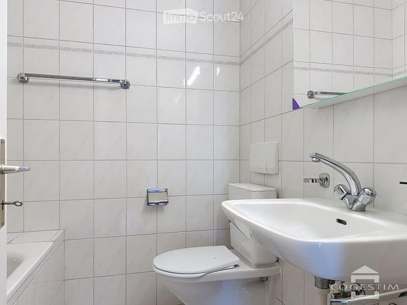Modern bathroom with white tiles, a toilet, a sink with a chrome faucet, a bathtub, and a mirror above the sink.