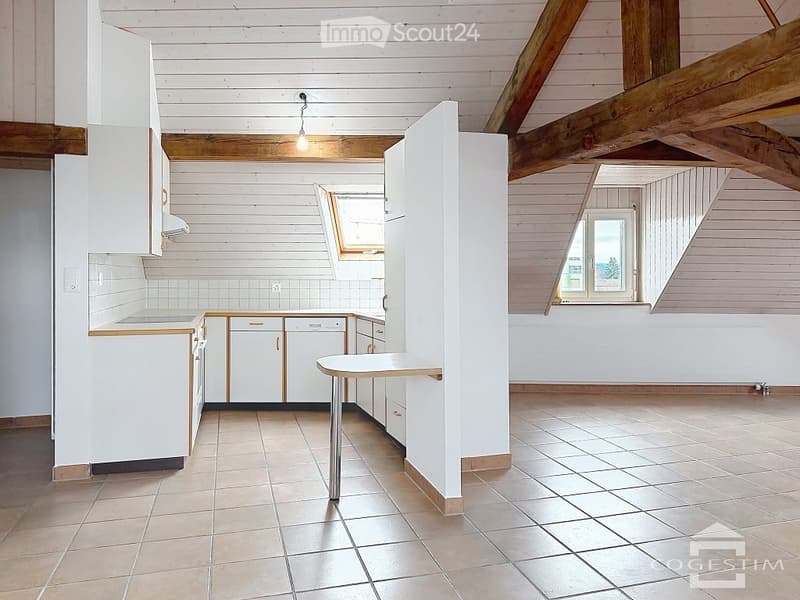 Bright kitchen with white cabinets, tiled floor, and wooden beams on the ceiling. Features a countertop, dishwasher, and a small table.