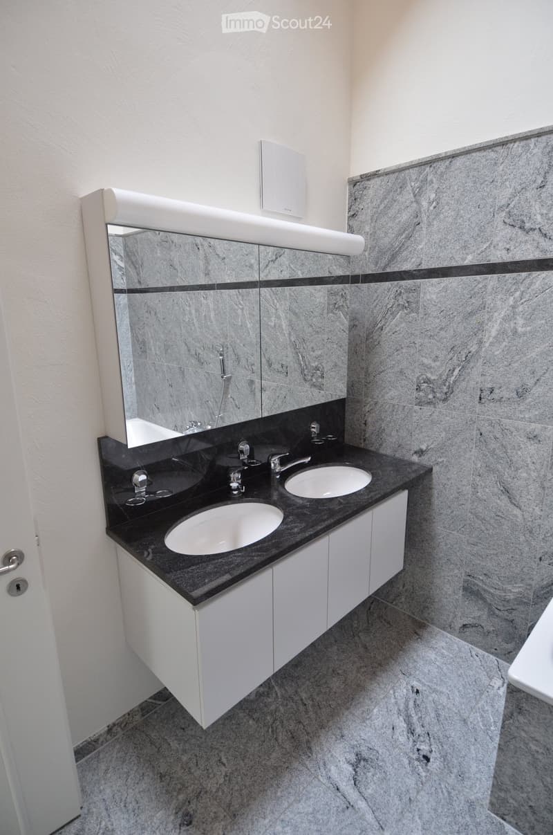 Modern bathroom with double sink vanity, black countertop, white cabinets, and large mirror.