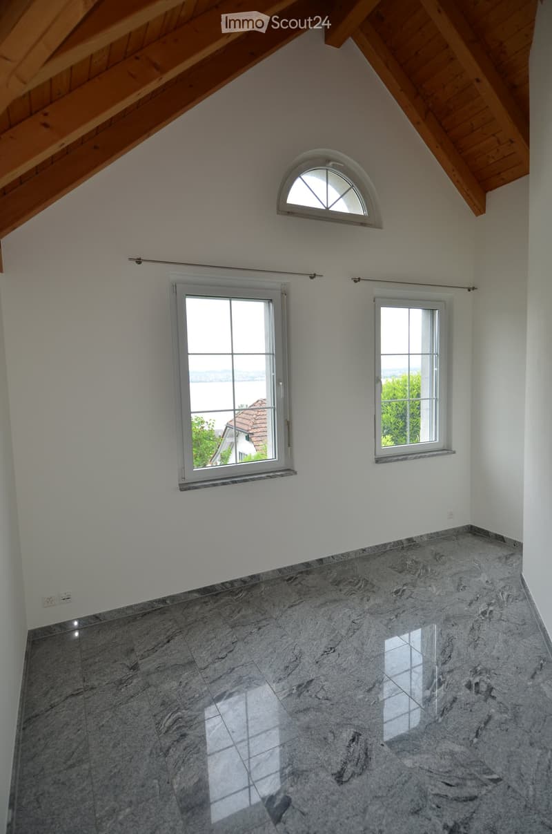 Empty room with marble flooring, white walls, and multiple windows including a skylight, offering natural light and a view.