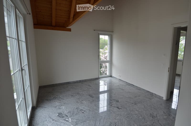 Empty room with polished marble flooring, white walls, large windows, and a wooden slanted ceiling.