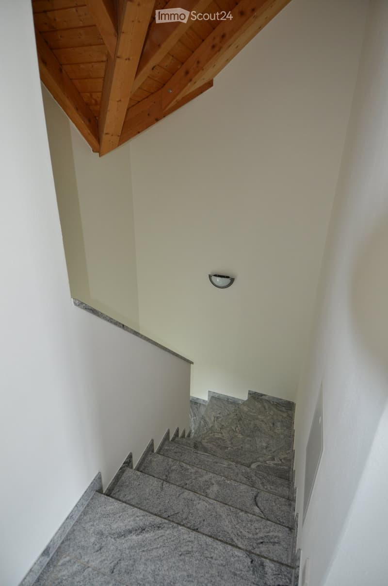 Staircase with marble steps and wooden handrail, light fixture on wall, wooden ceiling beams.