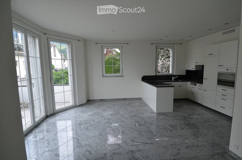 Modern kitchen with white cabinets, black countertop, marble flooring, and large windows letting in natural light.