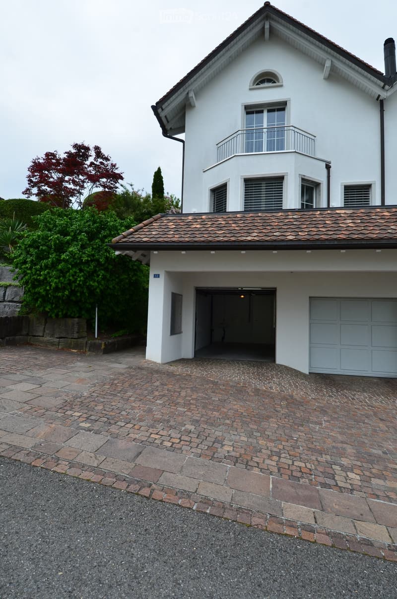 Two-story white house with a tiled roof, garage, and balcony on the upper level. The entrance has a brick-paved pathway leading to a double door.