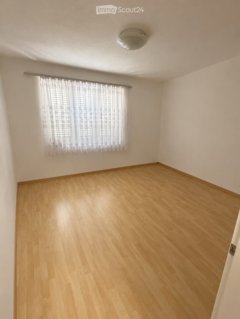 Empty room with wooden flooring, white walls, and a window with sheer curtains. No furniture or equipment is present.