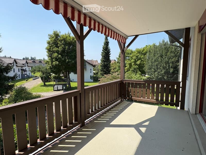 wooden railing, red and white striped awning, view of a grassy area with trees and houses