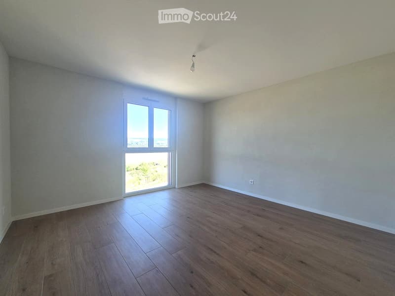 Empty room with wooden flooring, white walls, and large windows offering a scenic view.