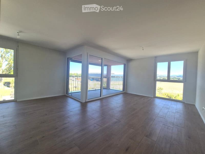 Empty room with wooden flooring, large windows, and sliding glass doors leading to a balcony with a scenic view.