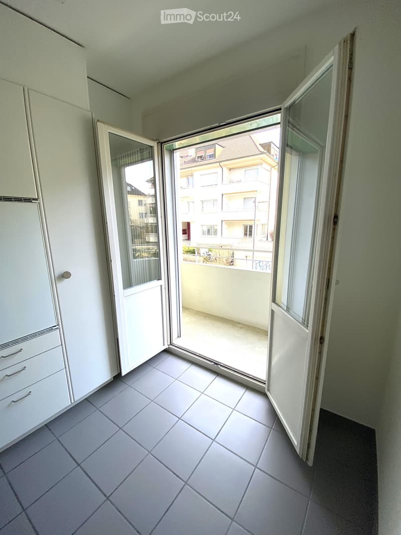 empty room with an opened door leading to a balcony, white tiled floor, white cabinet with drawers