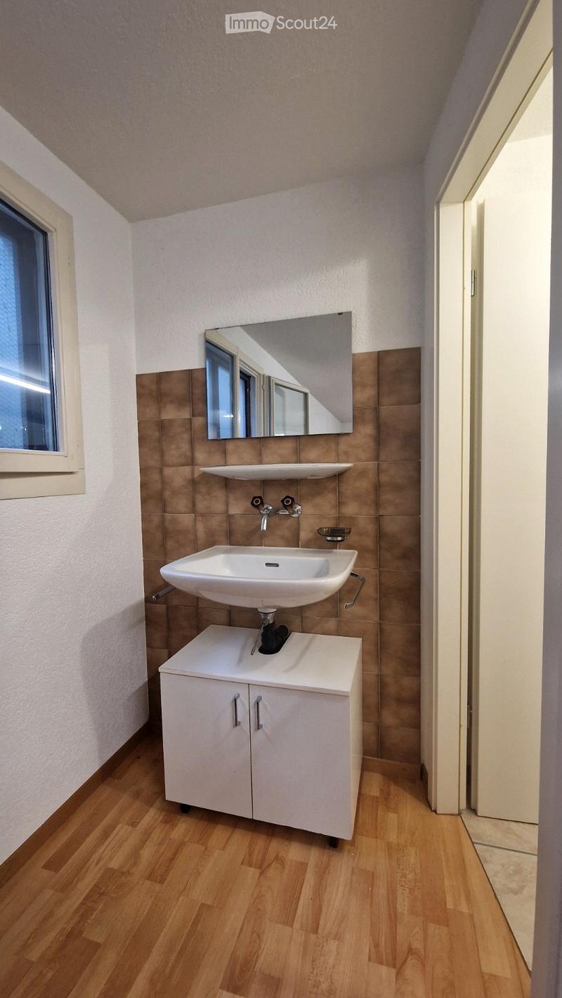 Modern bathroom with a white sink, mirror, and cabinet, featuring wooden flooring and tiled walls.