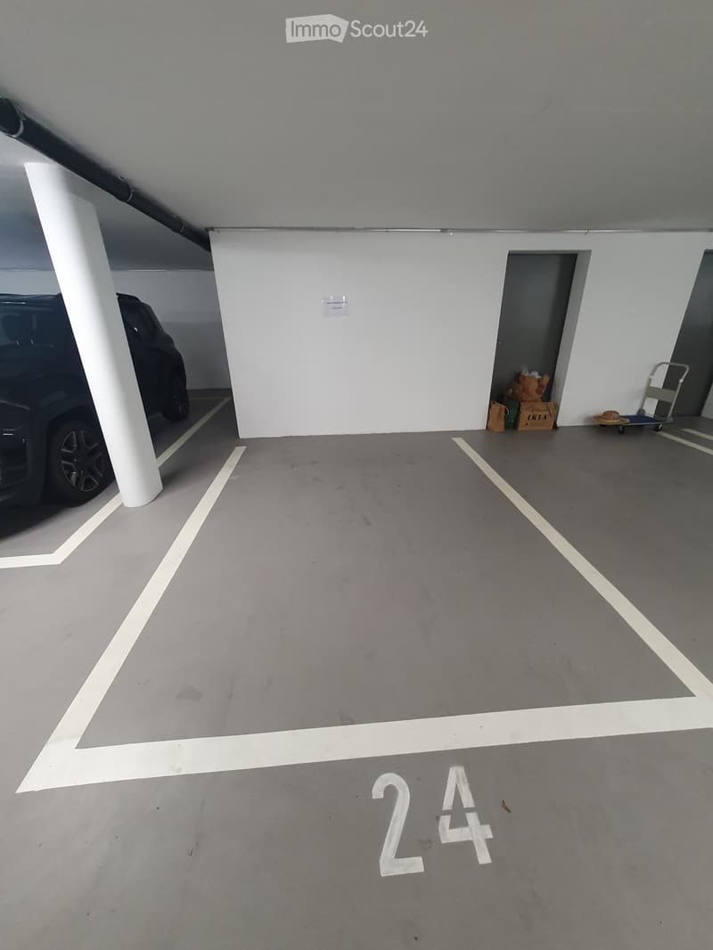 Underground parking area with marked spaces, a parked car, and storage items in a corner.