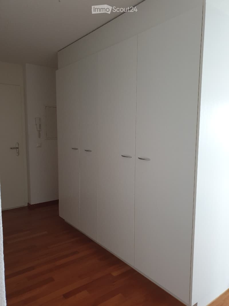 Empty room with white built-in wardrobes, wooden flooring, and a closed door visible in the background.