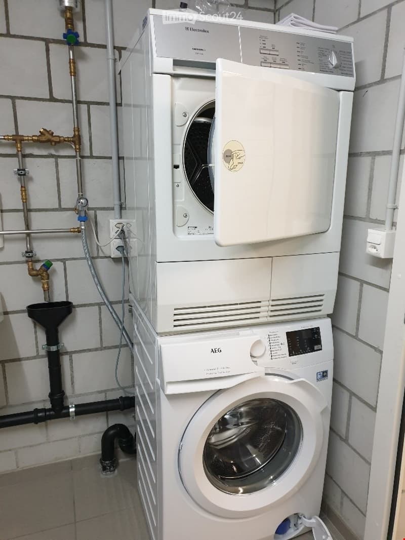 A compact bathroom with a stacked washing machine and dishwasher unit, white tiled walls, and visible plumbing.