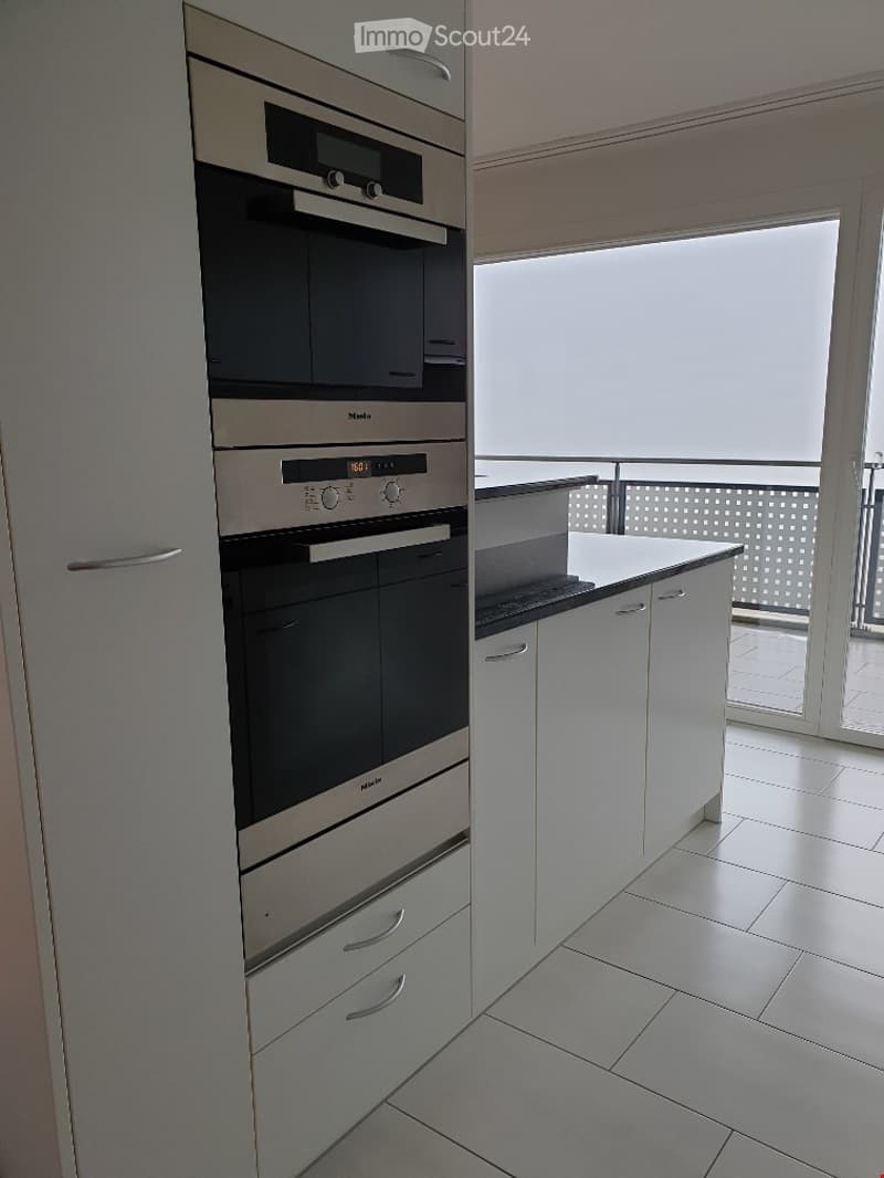 Modern kitchen with white cabinets, stainless steel oven, and a balcony view.