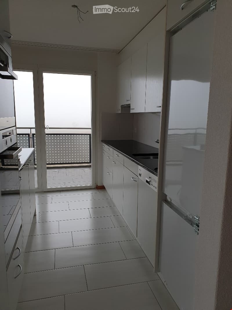 Modern kitchen with white cabinets, stainless steel appliances, and a large window leading to a balcony.