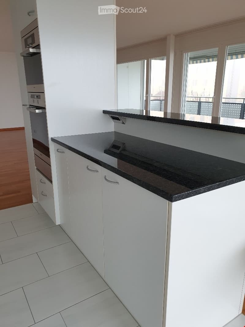 Modern kitchen with white cabinets, black countertop, and large windows overlooking a balcony.