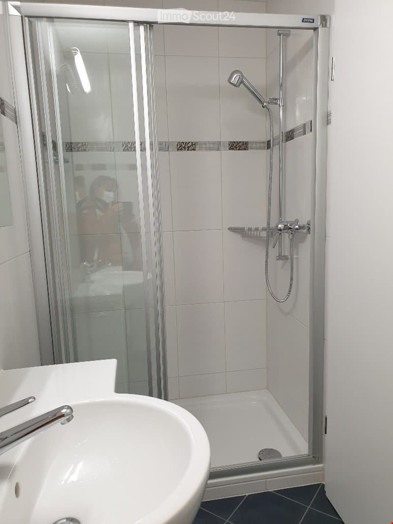 Modern bathroom with a white tiled shower stall, glass enclosure, and a white sink with a chrome faucet.