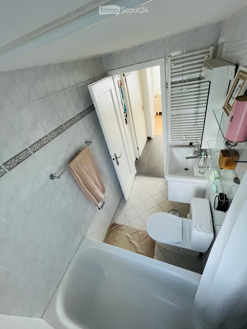 Bathroom with white tiles, bathtub, toilet, sink, mirror, and towels.