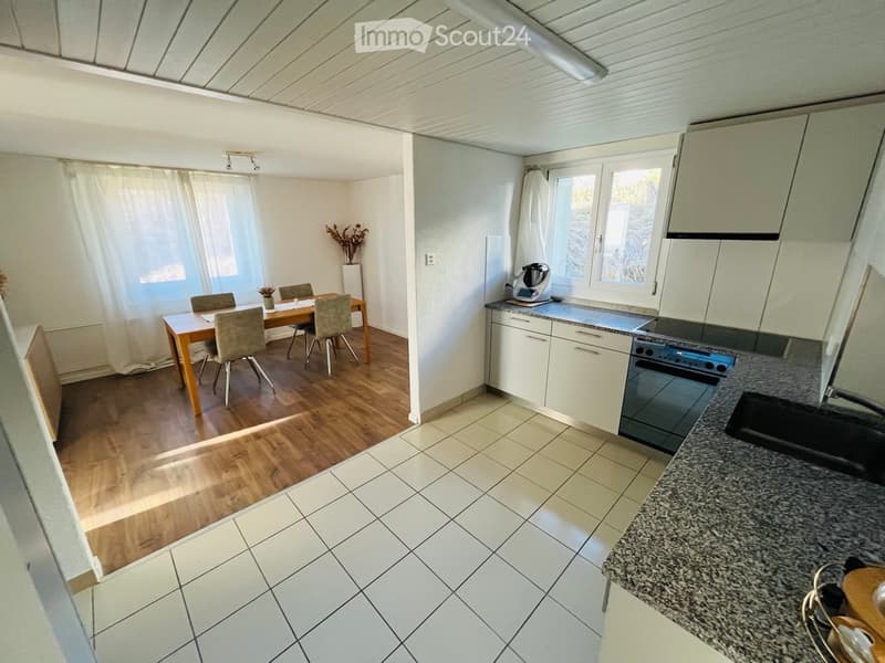 Open-plan kitchen and dining area with wooden flooring, white cabinets, granite countertop, and a dining table with four chairs.
