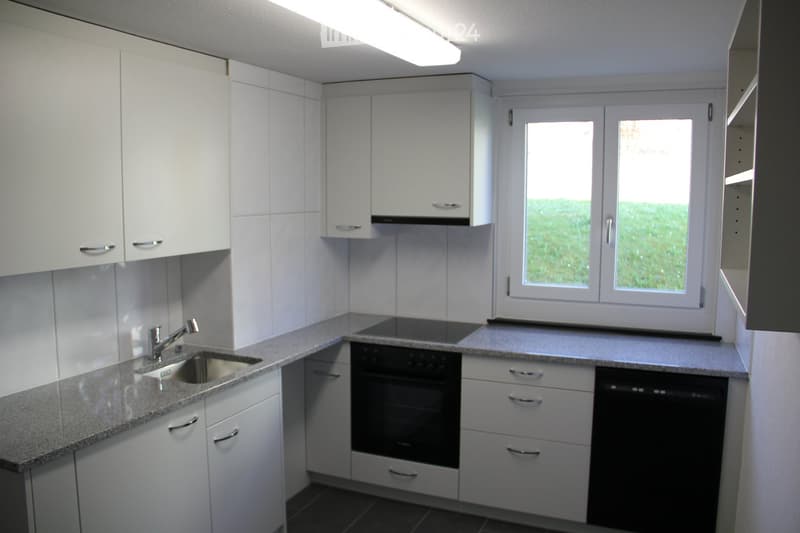 Modern kitchen with white cabinets, granite countertop, sink, oven, and dishwasher. Large window provides natural light.