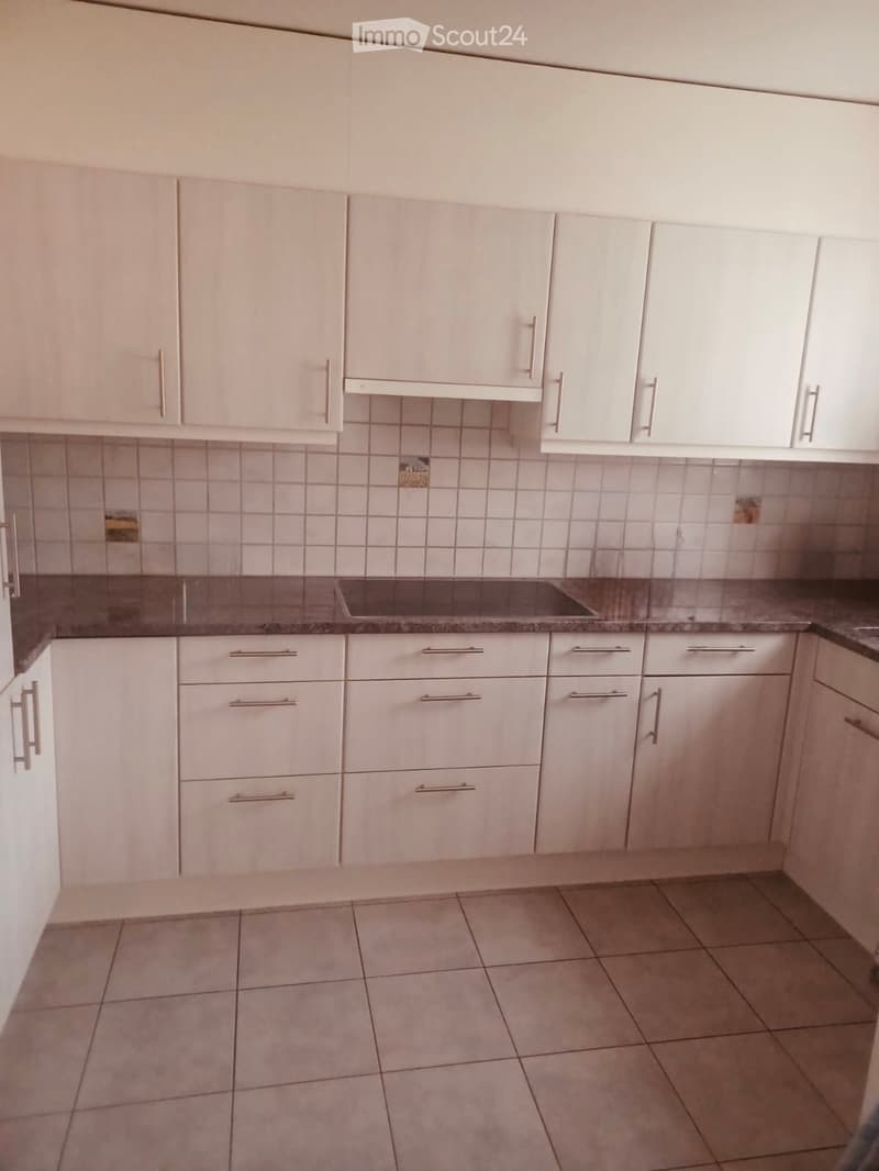 Empty kitchen with white cabinets, tiled walls, and a granite countertop.