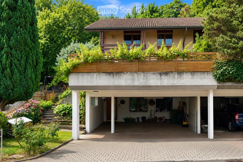 Two-story house with a tiled roof, balcony, garage, and garden area with greenery and flowers.