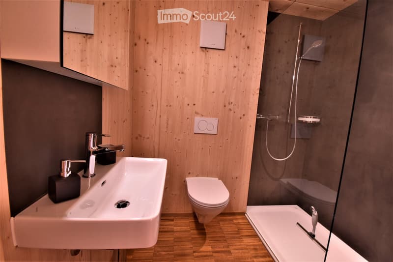 Modern bathroom with wooden walls, a white sink, a toilet, a bathtub, and a glass-enclosed shower area.