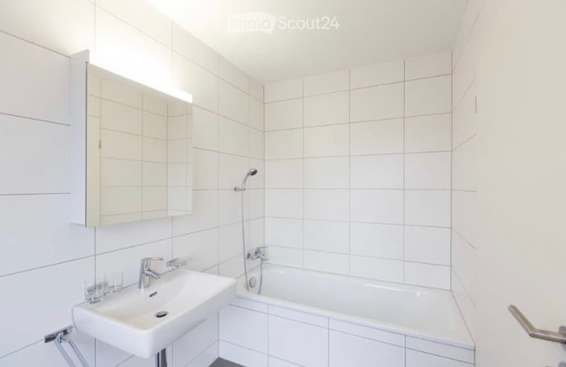 Modern bathroom with white tiled walls, a sink, bathtub, and a mirror cabinet.