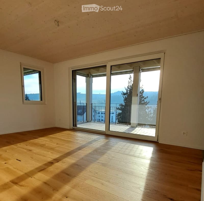 Empty room with wooden flooring, large sliding glass doors leading to a balcony, and a window on the left side.