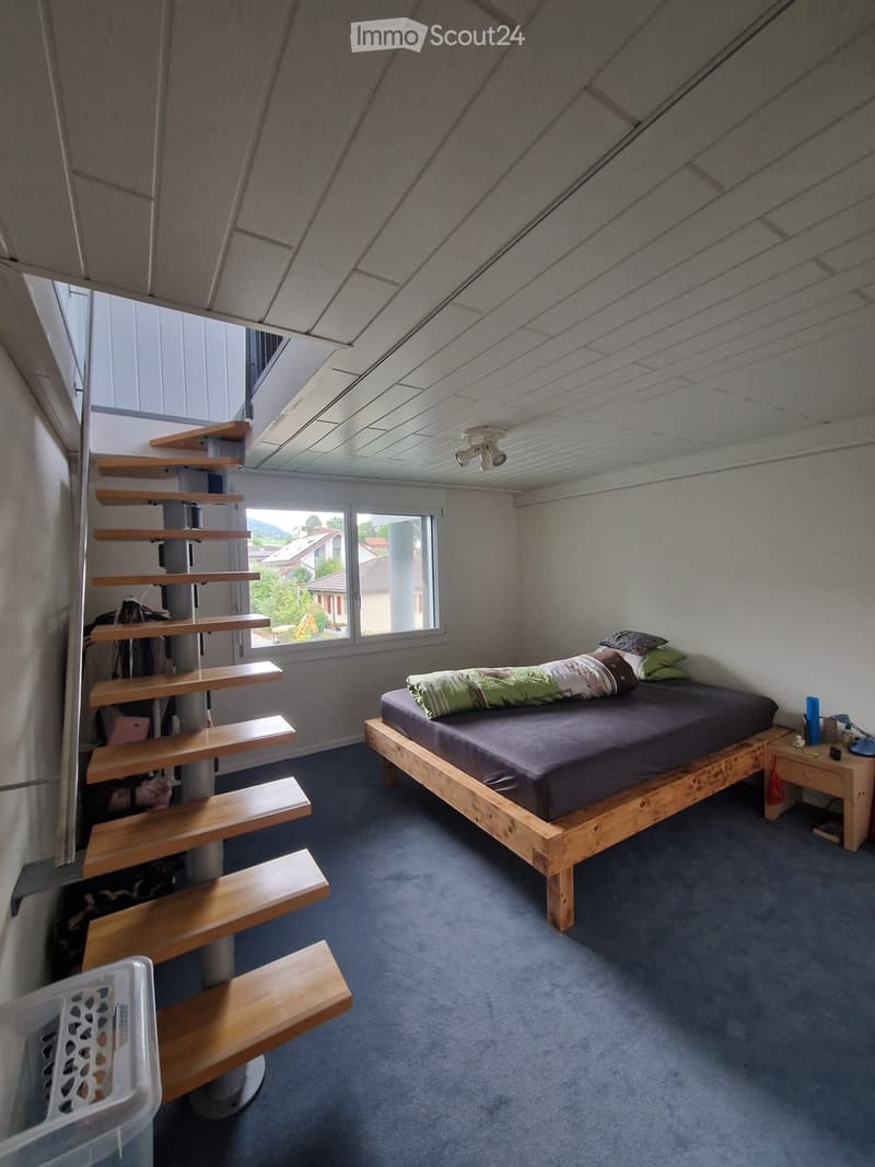 Bedroom with a wooden bed, nightstand, lamp, and a wooden staircase leading to an upper level.