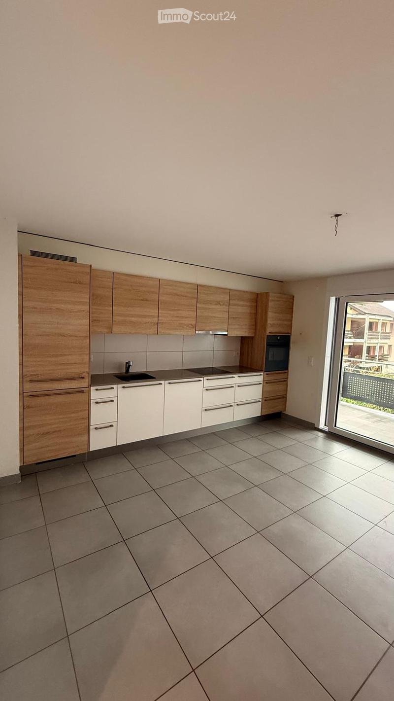 Modern kitchen with light wooden cabinets, white lower cabinets, tiled floor, and a large window with a view of the outdoor area.
