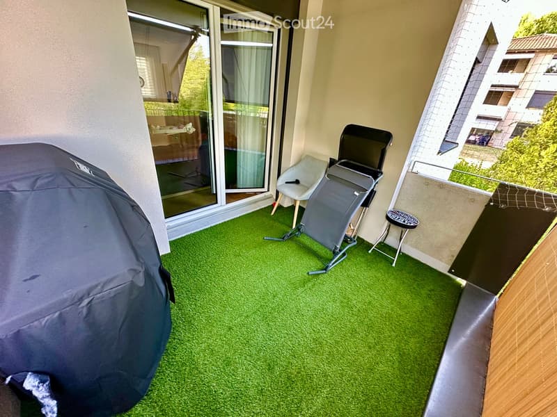 Balcony with artificial grass flooring, a covered grill, a chair, a small stool, and a massage table.