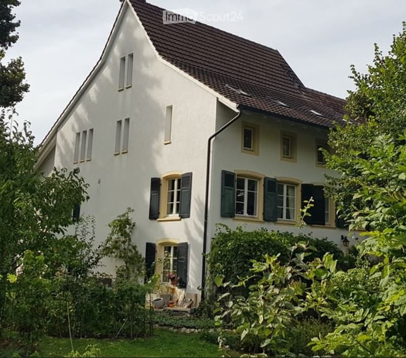 Two-story white house with a brown tiled roof, multiple windows with shutters, and a well-maintained garden in front.