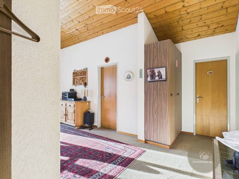 A furnished room with a wooden ceiling, a cabinet, a screen, a table, a chair, a mirror, and a door.