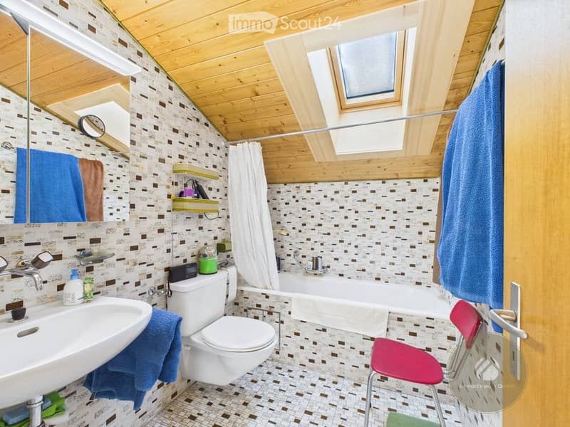 Bathroom with wooden ceiling, patterned tiles, sink, toilet, bathtub, mirror, and a small chair.