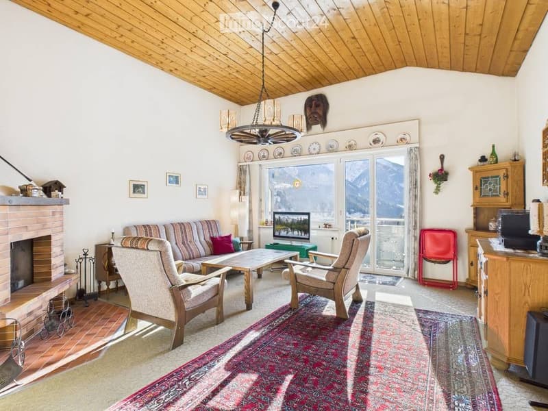 Cozy living room with a fireplace, large window offering a mountain view, sofa, armchairs, coffee table, television, and decorative items.