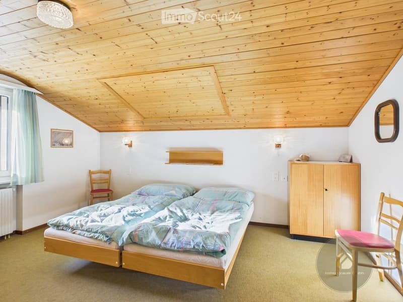 Cozy bedroom with wooden slanted ceiling, two single beds, a wooden chair, a small cabinet, and a mirror on the wall.
