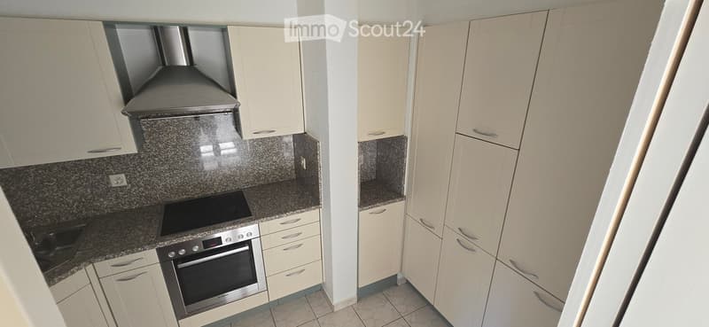 Modern kitchen with light-colored cabinets, granite countertops, and stainless steel appliances including an oven and induction cooktop.