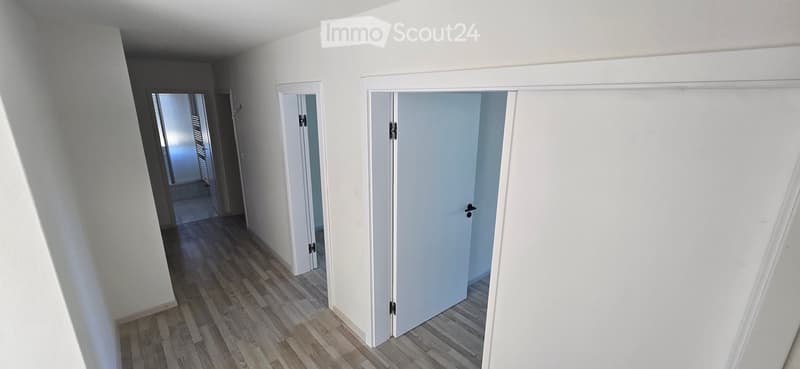 Empty hallway with white walls, wooden flooring, and multiple closed doors leading to other rooms.