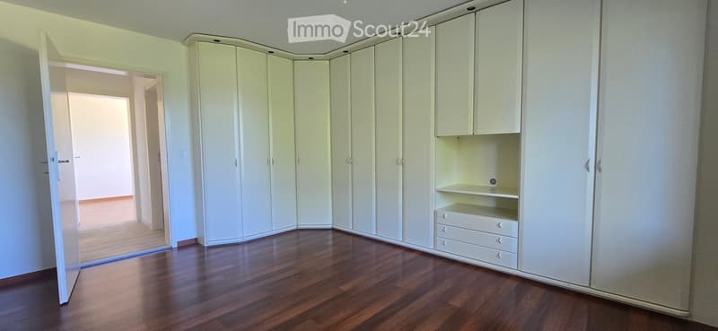 Empty room with light-colored walls, wooden flooring, and built-in white wardrobes with drawers and shelves.