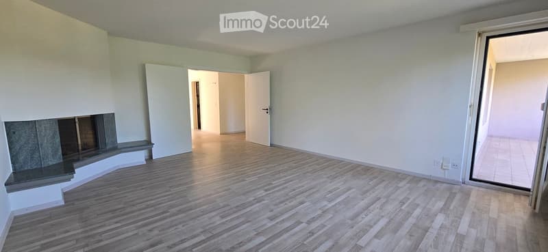 Empty room with wooden flooring, white walls, and a fireplace on the left side. There are two open doors leading to other rooms.