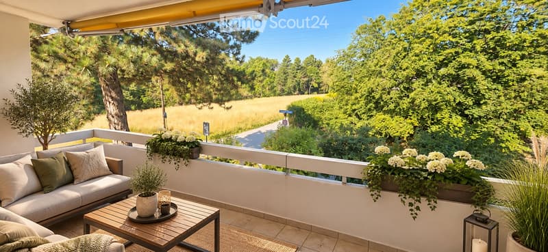 Balcony with a view of a green landscape, featuring a sofa, coffee table, potted plants, and candle holders.