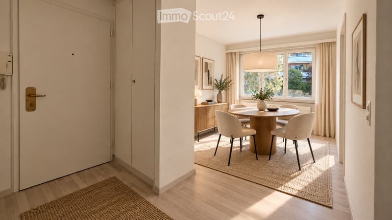 Modern dining area with a round wooden table surrounded by six light-colored chairs, a pendant light fixture, a sideboard with a vase and picture frames, and natural light from large windows.