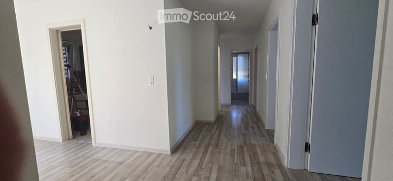Empty hallway with wooden flooring, white walls, and multiple doors leading to other rooms.