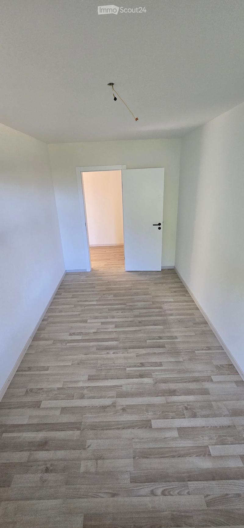 Empty room with light grey walls, wooden flooring, and a white door leading to another room.