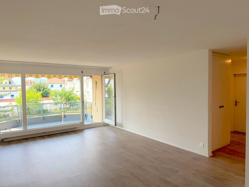 Empty room with light-colored walls, wooden flooring, and large sliding glass doors leading to a balcony.
