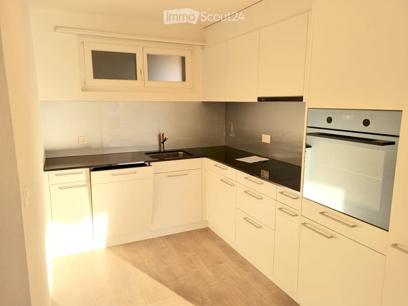 Modern kitchen with white cabinets, black countertops, and stainless steel appliances including a sink, faucet, and oven.