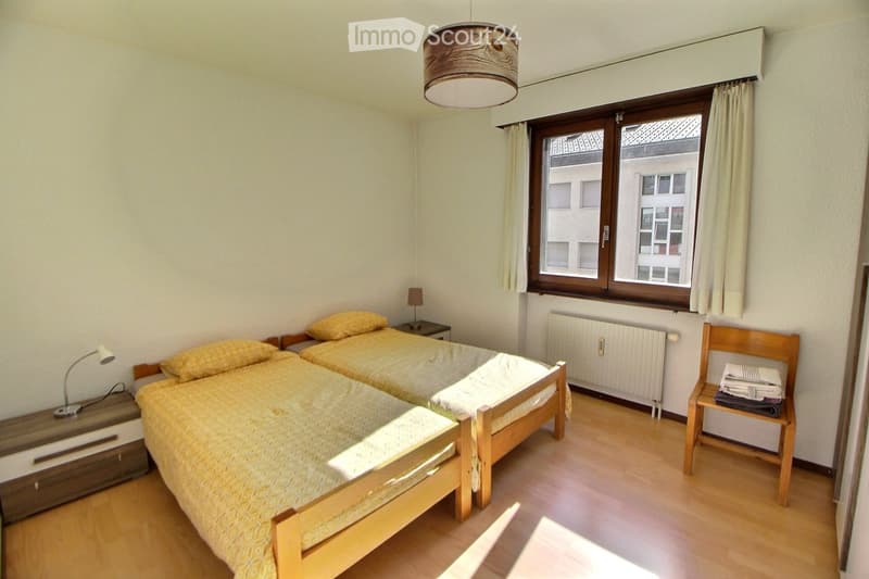 Cozy bedroom with two single beds, wooden nightstands, a wooden chair with folded towels, and a window with curtains.