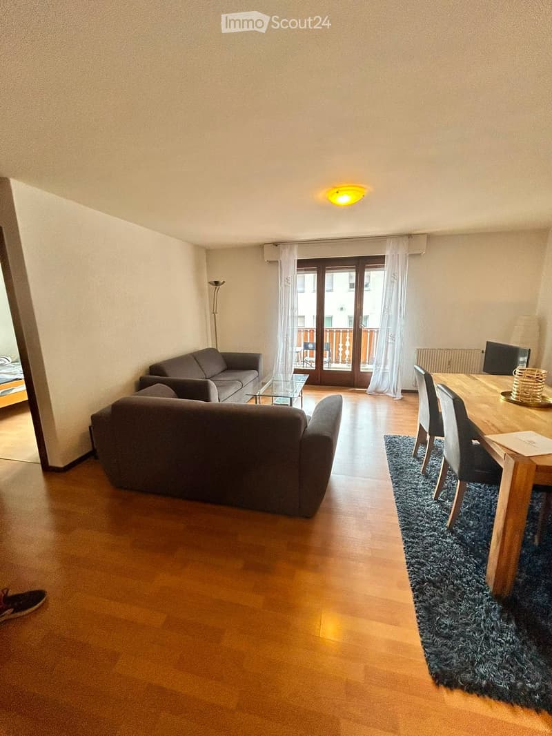 Living room with wooden floor, sofa, coffee table, dining table, chairs, screen, and floor lamp. Access to a balcony.